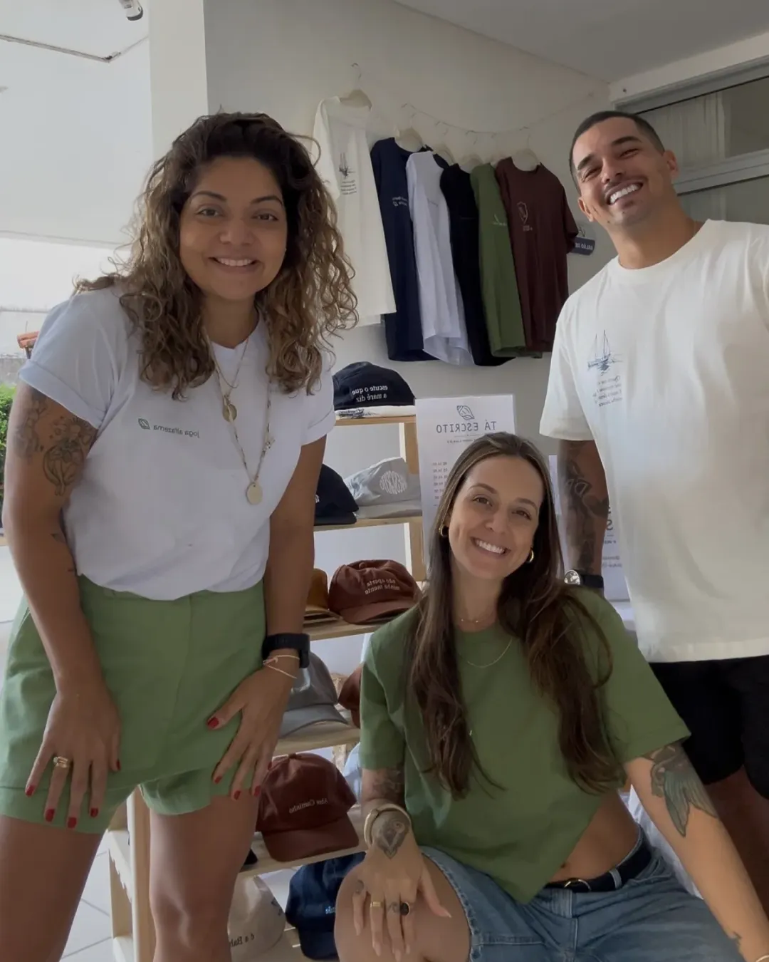 As pessoas por trás da Tá Escrito com as camisetas e os bonés da marca numa feira em Salvador